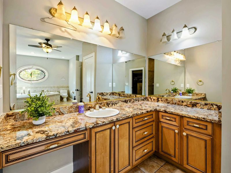 Primary Bath - An L-shaped granite vanity with dual sinks, large mirror, and warm lighting.