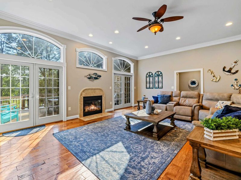 Living Room - Floor-to-ceiling arched windows, hardwood floors, and a sectional arranged around the fireplace with pool views outside.