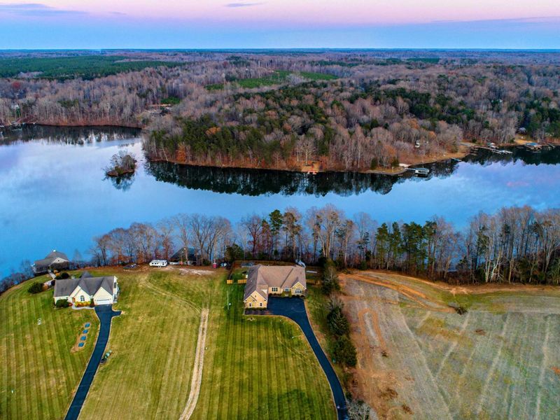 Aerial - A winter twilight drone shot showing the property, neighbor, and lake beyond under pink and blue skies.