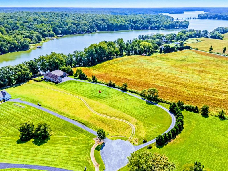 Aerial - The full 2.63-acre property from above: rolling fields, the stone home, and the lake wrapping around the shoreline.