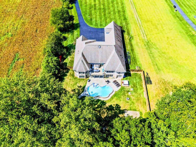 Aerial - Directly above the home: the pool, fenced backyard, stone facade, and three-car garage all visible.