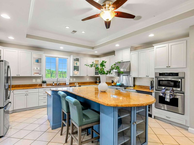 Kitchen - A blue island with granite counters and bar seating anchors the kitchen, with stainless appliances and white cabinetry all around.