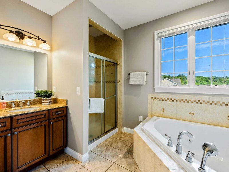 Ensuite 2 Bath - A jacuzzi tub and glass-enclosed shower with granite vanity and natural light from the window.