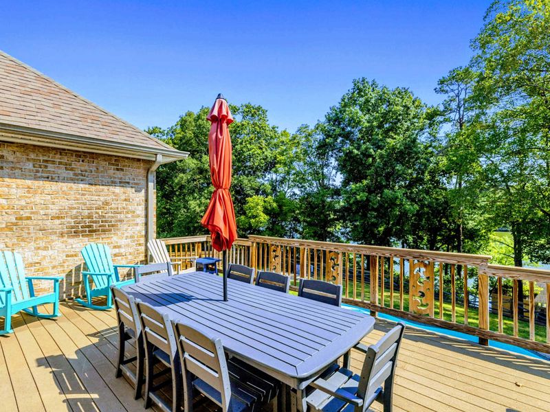 Deck Dining - A full outdoor table with umbrella and Adirondack rockers on the upper deck, surrounded by trees.