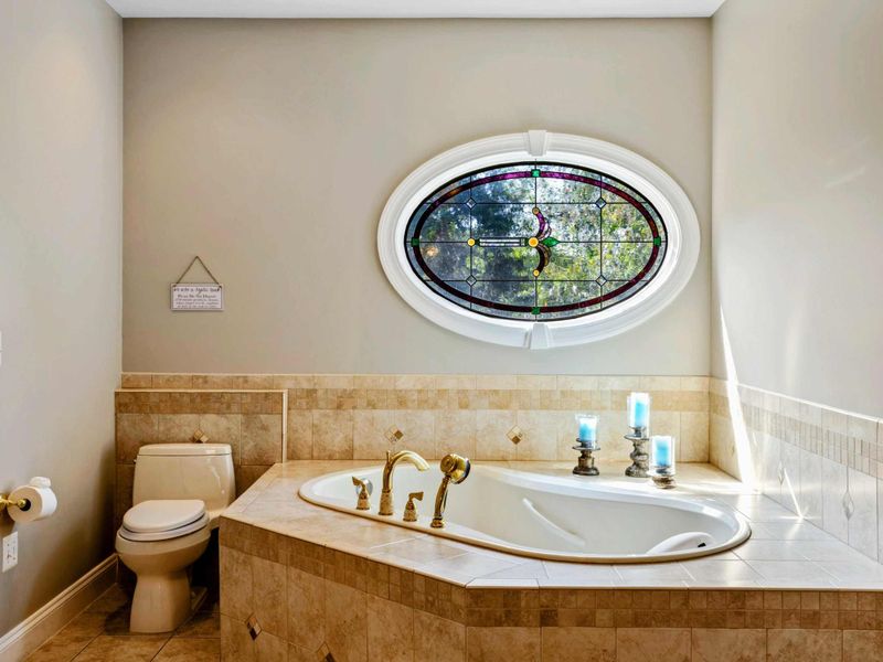 Primary Bath - Closer view of the soaking tub and stained glass window, with gold hardware throughout.