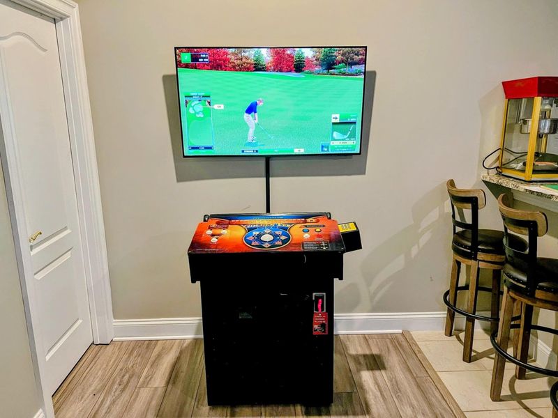 Game Room - A Golden Tee arcade cabinet with a mounted TV, steps from the bar area.