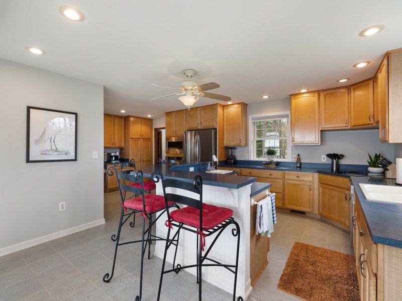 An open-plan kitchen with wooden cabinets, modern appliances, and a cozy breakfast bar with stylish red stools