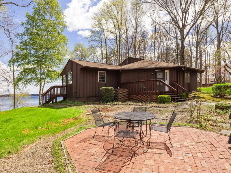 A welcoming cabin with an outdoor patio area nestled by the lake, framed by tall trees and fresh greenery