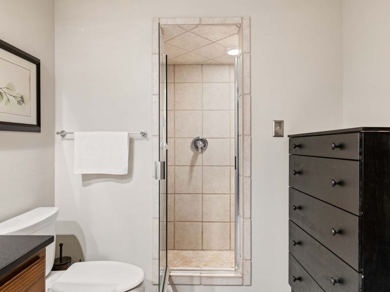 A clean and sophisticated bathroom with a large mirror, wood vanity, and a glass-enclosed shower