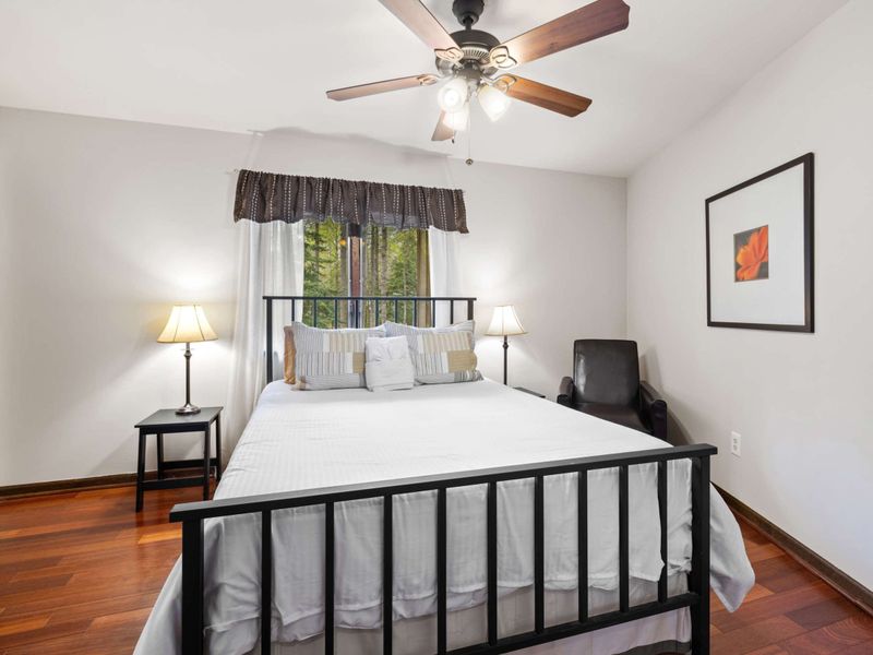 A simple and inviting bedroom with a ceiling fan, comfortable bedding, and warm wooden floors