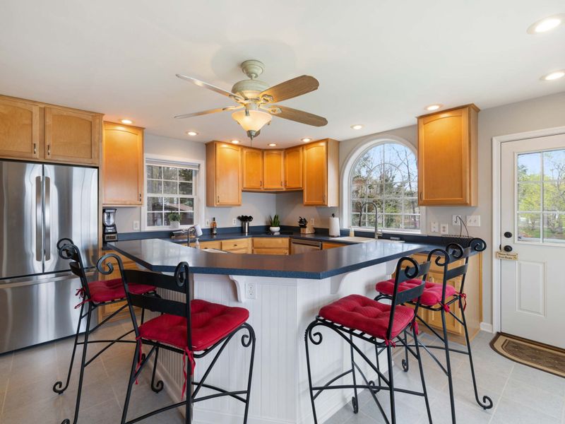 An open-plan kitchen with wooden cabinets, modern appliances, and a cozy breakfast bar with stylish red stools
