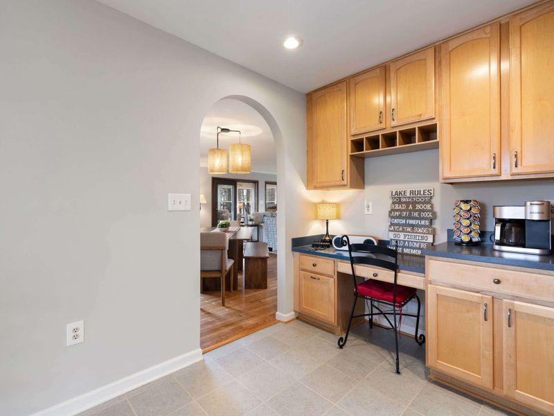 An inviting kitchen nook with a quirky "Lake Rules" sign, wood cabinetry, and a peek into the cozy dining area