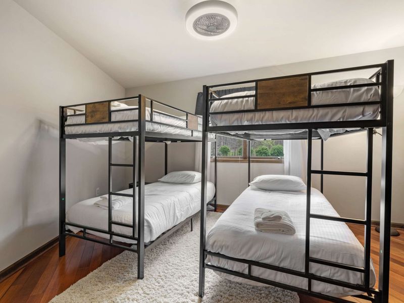 A room equipped with two bunk beds, ideal for multiple guests, featuring large windows and hardwood floors