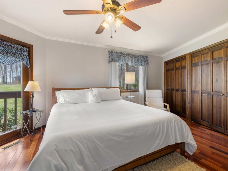 A bright and Primary bedroom with a comfortable bed, hardwood floors, and a view of nature through large windows