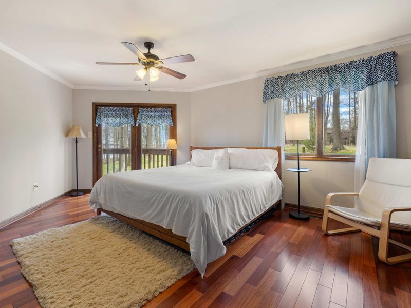 A bright and cozy bedroom with a comfortable bed, hardwood floors, and a view of nature through large windows