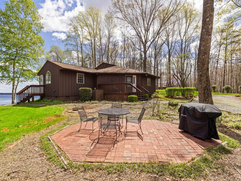 A welcoming cabin with an outdoor patio area nestled by the lake, framed by tall trees and fresh greenery