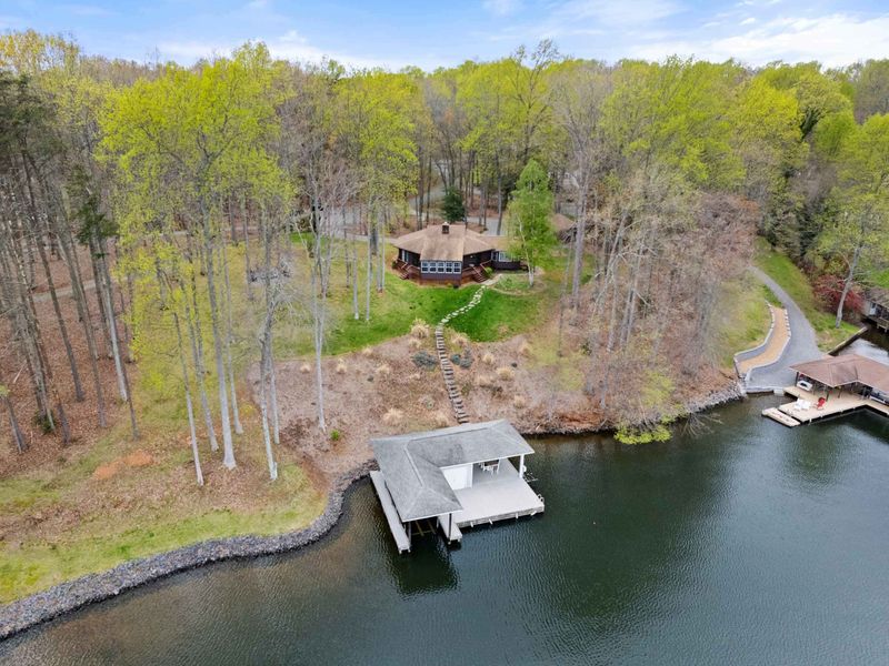 An aerial snapshot captures a secluded cabin retreat by a serene lake, complete with a private dock amidst a forested landscape