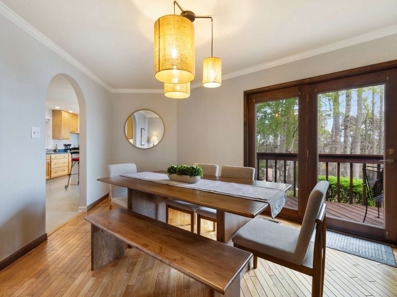 Chic dining space with a natural wood table, ambient lighting, and balcony access offering a tranquil forest backdrop