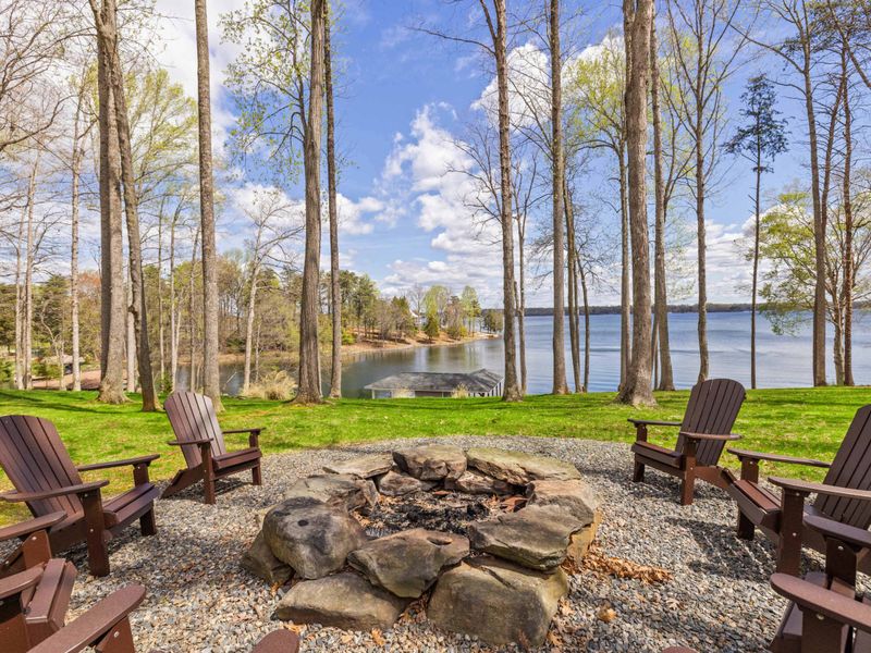 A relaxing fire pit area with Adirondack chairs overlooking a serene lake, nestled among tall trees