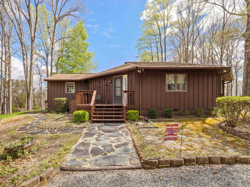 A charming, single-story brown house with a welcoming front porch set amidst a tranquil, wooded landscape