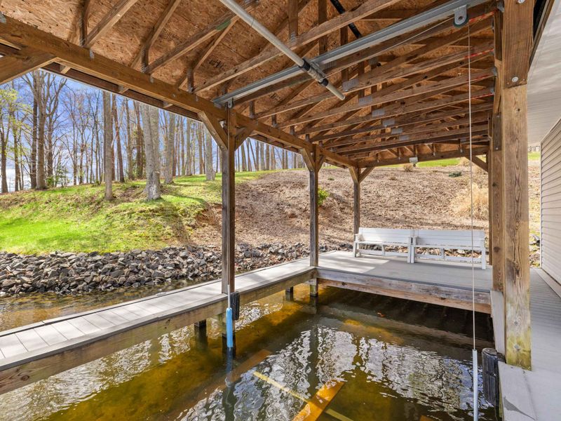 Under the shade of a wooden deck structure, this serene lakefront spot with a bench awaits visitors for a moment of lakeside tranquility