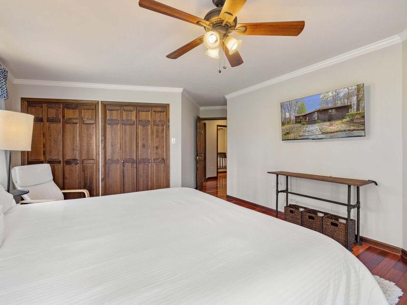 A tranquil bedroom featuring a large bed, wooden furniture, and a ceiling fan, with a touch of rustic charm
