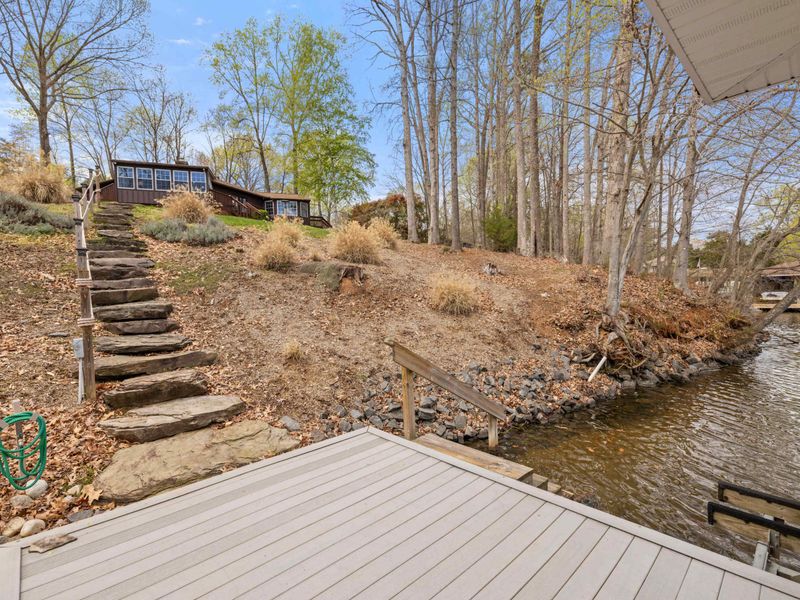 A tranquil lakeside scene with a rustic stone staircase leading up to a cozy woodland cabin