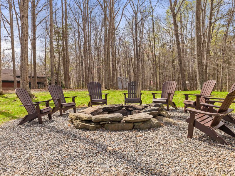 An inviting outdoor fire pit surrounded by wooden Adirondack chairs set in a tranquil forest clearing