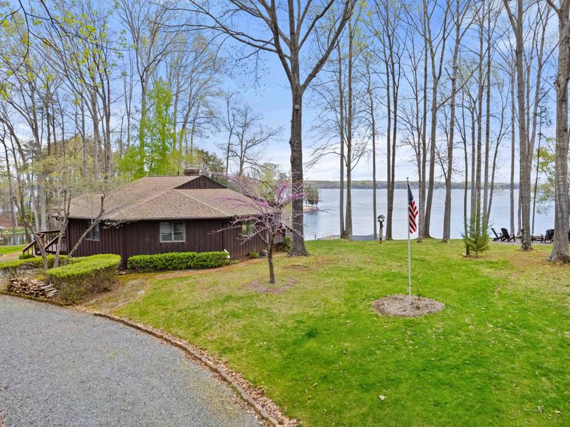 A peaceful lakeside retreat surrounded by trees, featuring a winding driveway and a waterfront view