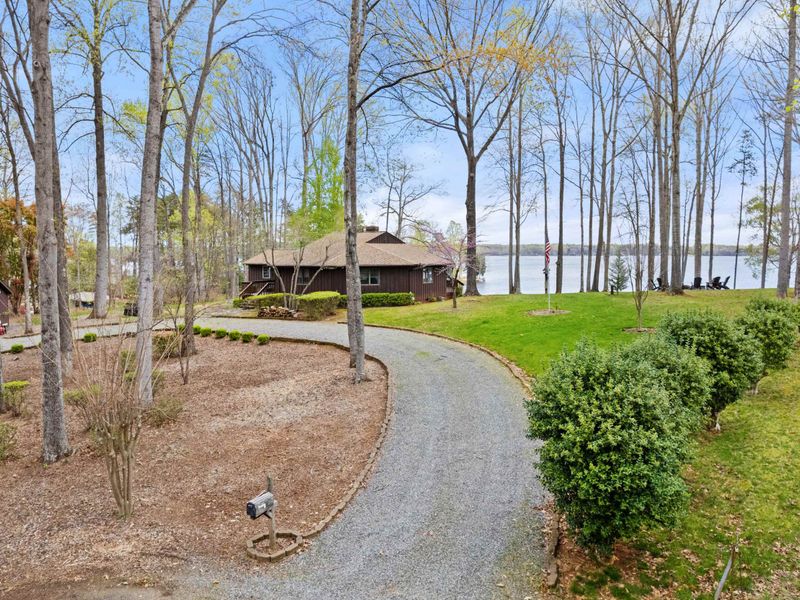 A peaceful lakeside retreat surrounded by trees, featuring a winding driveway and a waterfront view