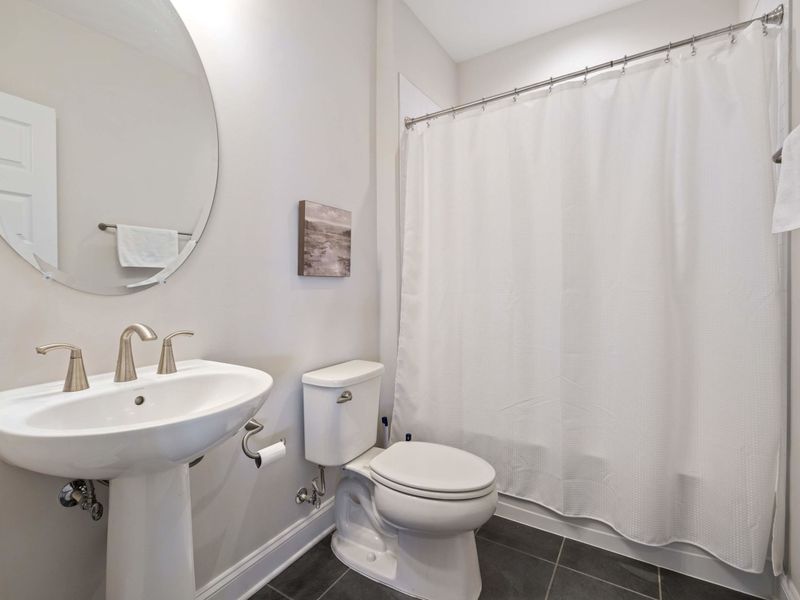 Full Bathroom - A compact but bright shared bath with pedestal sink, round mirror, and tub-shower combo.