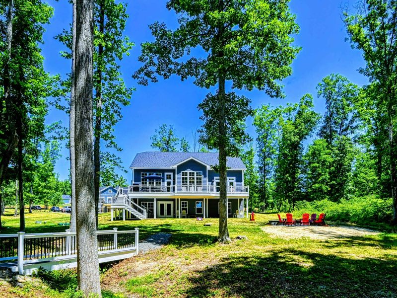Spacious lakeside house with a large deck and a cozy fire pit area, surrounded by lush trees