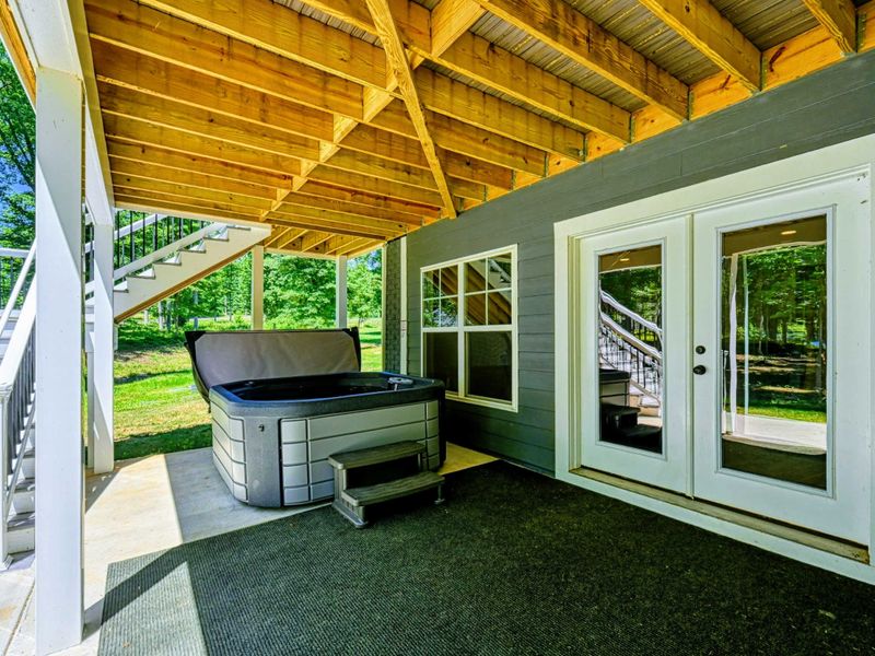 Covered patio area featuring a relaxing hot tub with wooded views.
