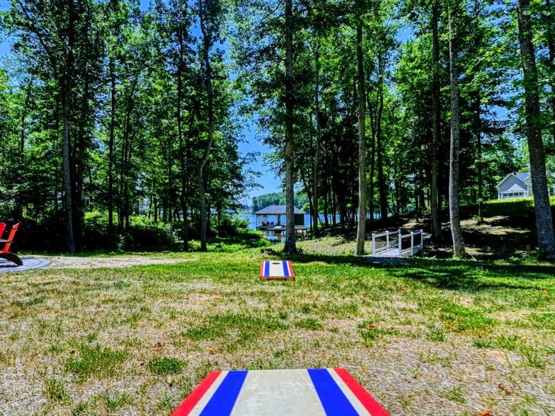 Cornhole game setup in a shaded backyard with a view of the lake and dock in the distance.