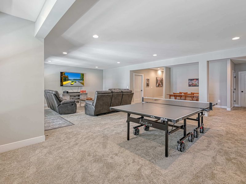 Spacious entertainment room featuring a ping pong table, comfortable seating, and a large TV