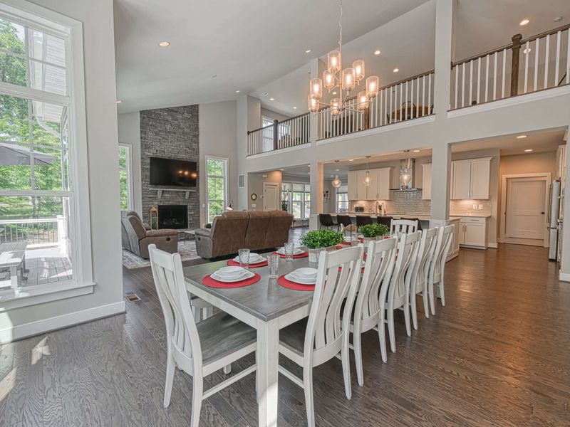 Elegant dining area with a large table set for a gathering, adjacent to an open-concept living room with high ceilings and modern decor.
