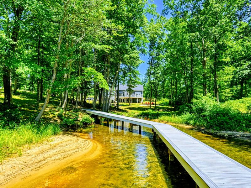 Scenic view of a house nestled in the woods with a private walkway leading to a clear, sandy beach and serene waters