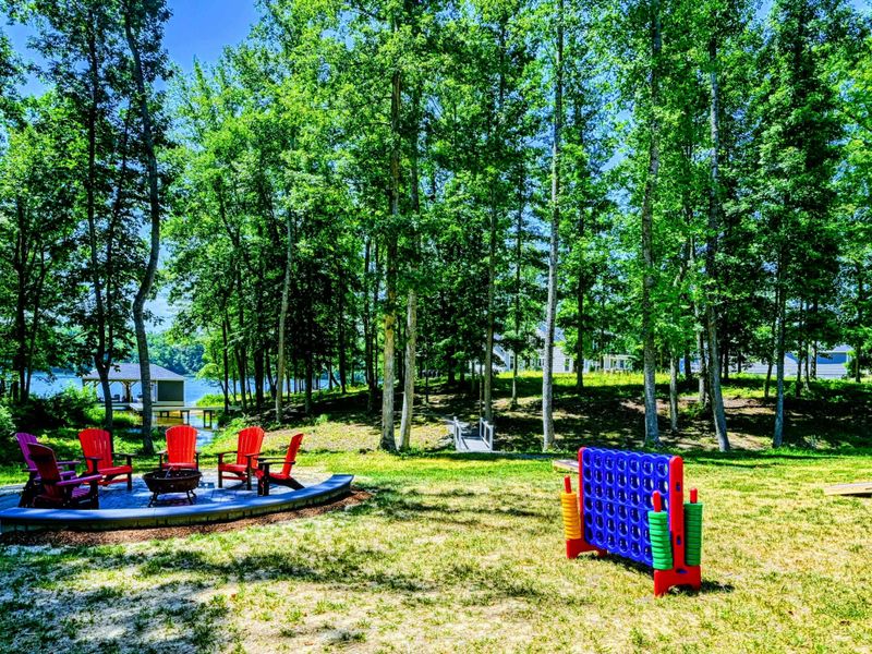Scenic backyard with a lakeside view, vibrant Adirondack chairs around a fire pit, and fun outdoor games