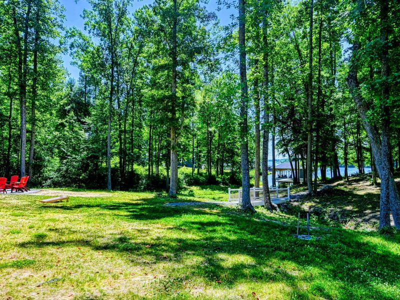 A serene backyard with a fire pit, cornhole game, and a path leading to a private dock on the lake.