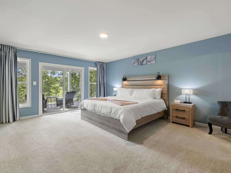A spacious and serene bedroom with a king-size bed, elegant decor, and large windows opening to a private balcony with lush views.