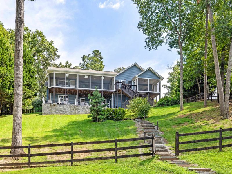 A stunning lakefront home with a spacious screened porch, surrounded by a lush green lawn and a charming stone pathway leading down to the water.