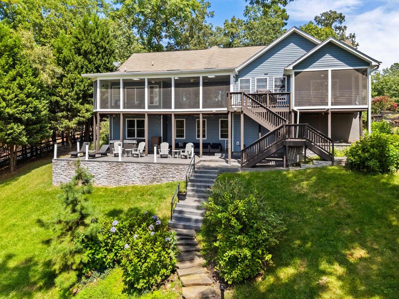 A stunning lakefront home with a spacious screened porch, surrounded by a lush green lawn and a charming stone pathway leading down to the water.