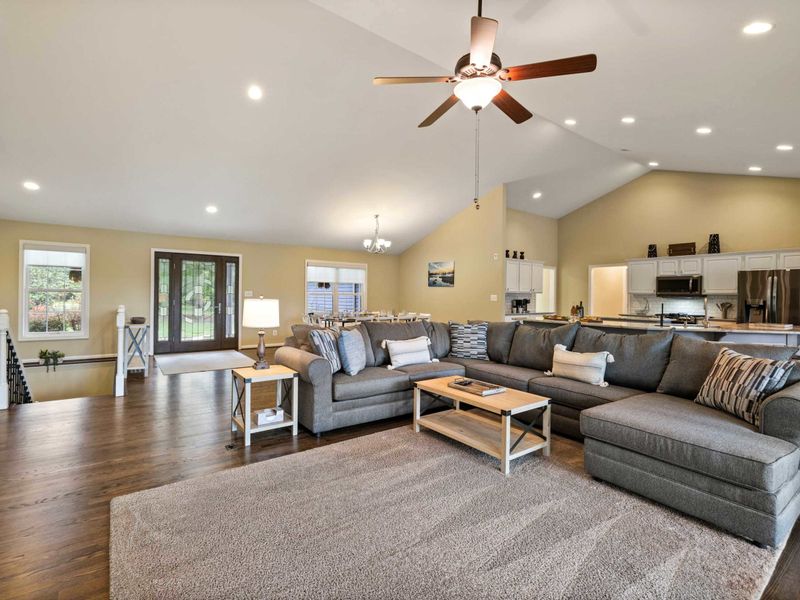 An inviting open-concept living space with a cozy sectional sofa, high ceilings, and a modern kitchen, perfect for gathering and relaxation.