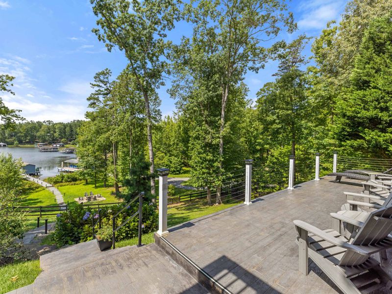 A spacious deck with Adirondack chairs overlooking a beautifully landscaped yard and a tranquil lake, perfect for relaxing and taking in the view.