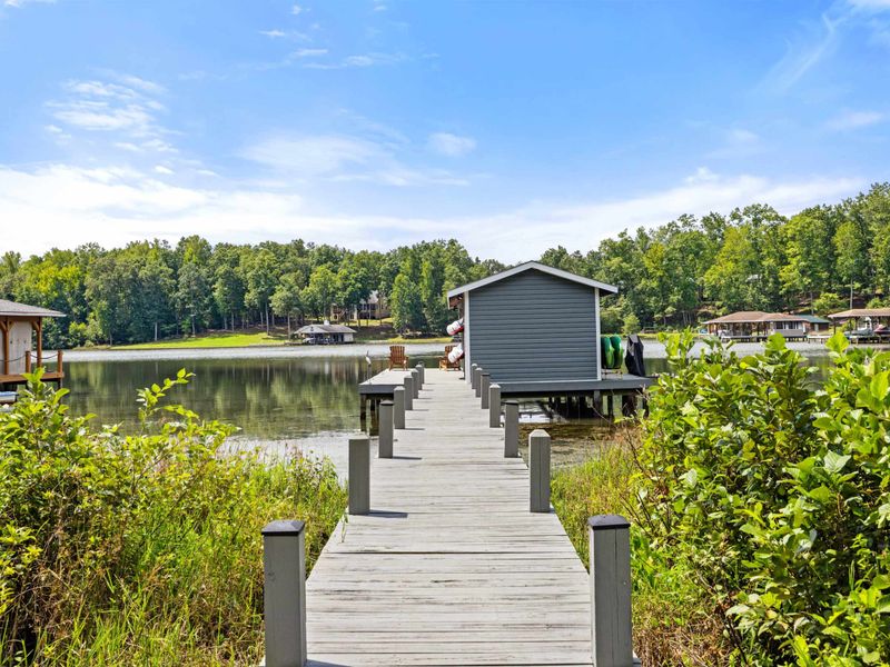 A private boardwalk leading to a covered dock on a peaceful lake, surrounded by lush greenery and offering a serene retreat.