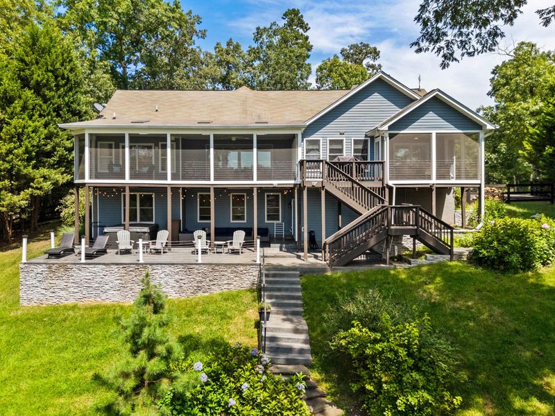 A stunning lakefront home with a spacious screened porch, surrounded by a lush green lawn and a charming stone pathway leading down to the water.