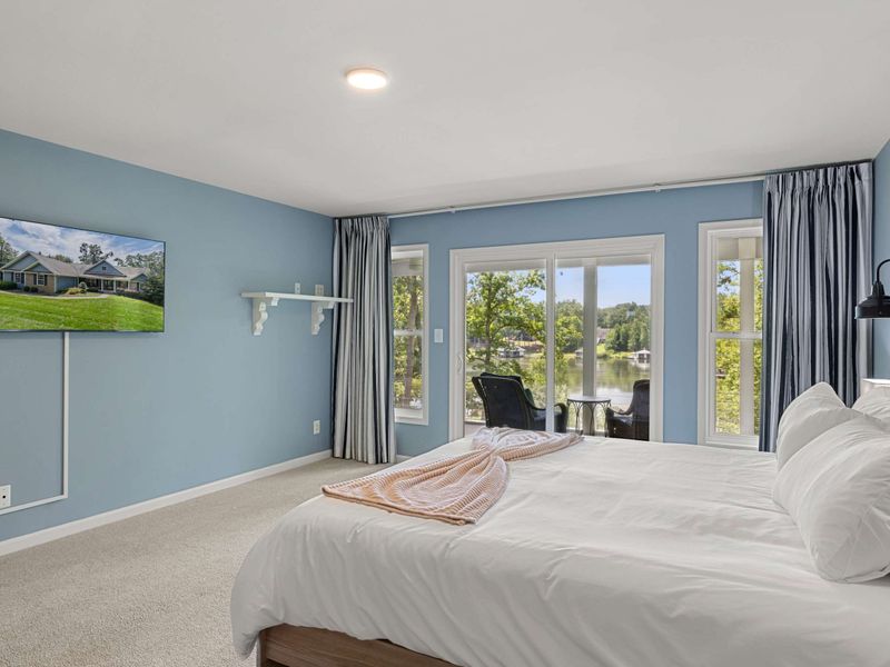 A spacious and serene bedroom with a king-size bed, elegant decor, and large windows opening to a private balcony with lush views.