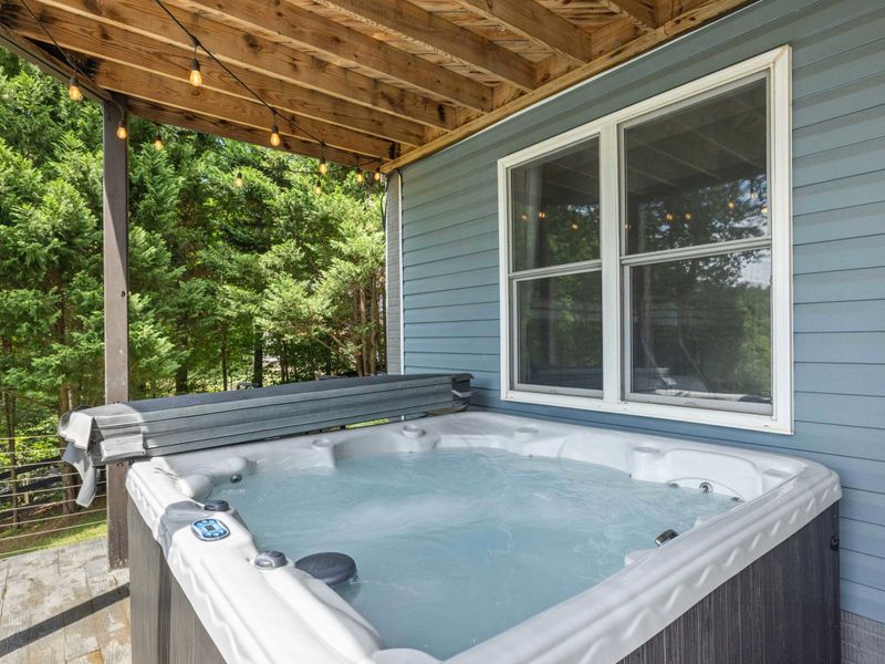 A private hot tub on a covered patio surrounded by lush greenery, perfect for unwinding in a tranquil lakeside setting.