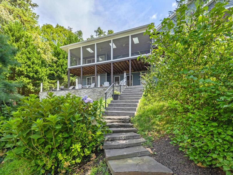 A beautifully designed lakefront home with a screened porch and stone walkway, surrounded by lush greenery for a peaceful retreat.