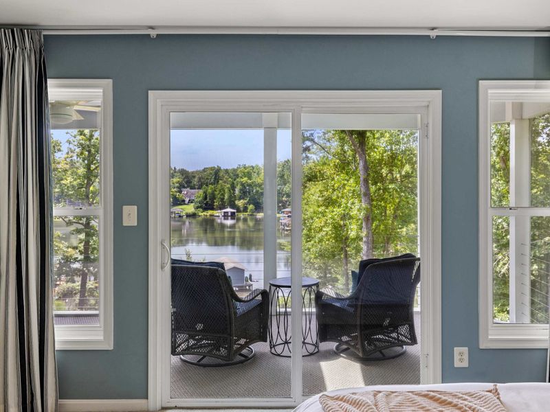 A tranquil bedroom view featuring sliding doors that open to a private balcony with cozy seating and picturesque lake views.